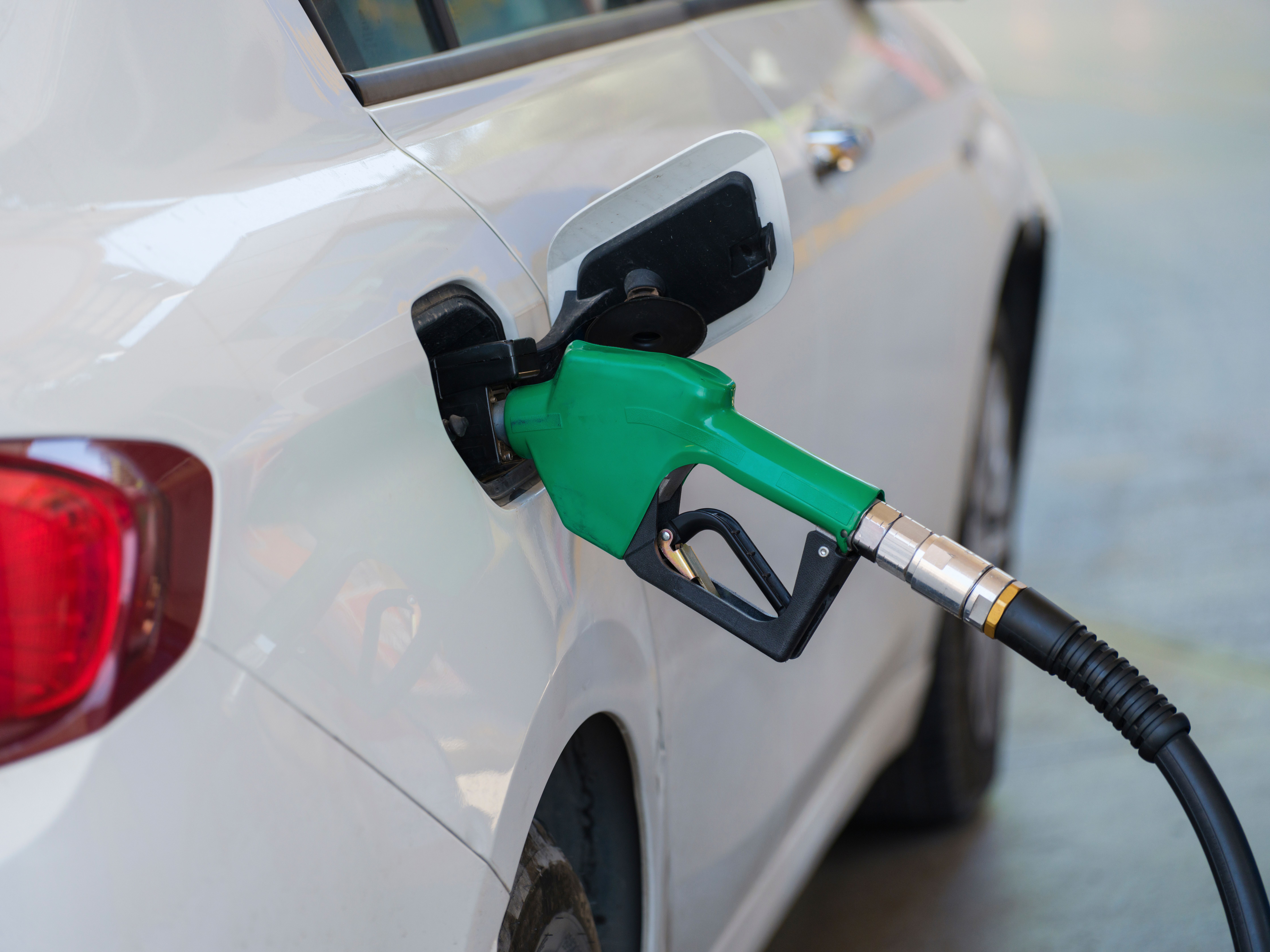 Close-up of a green nozzle refueling a white car at a gas station