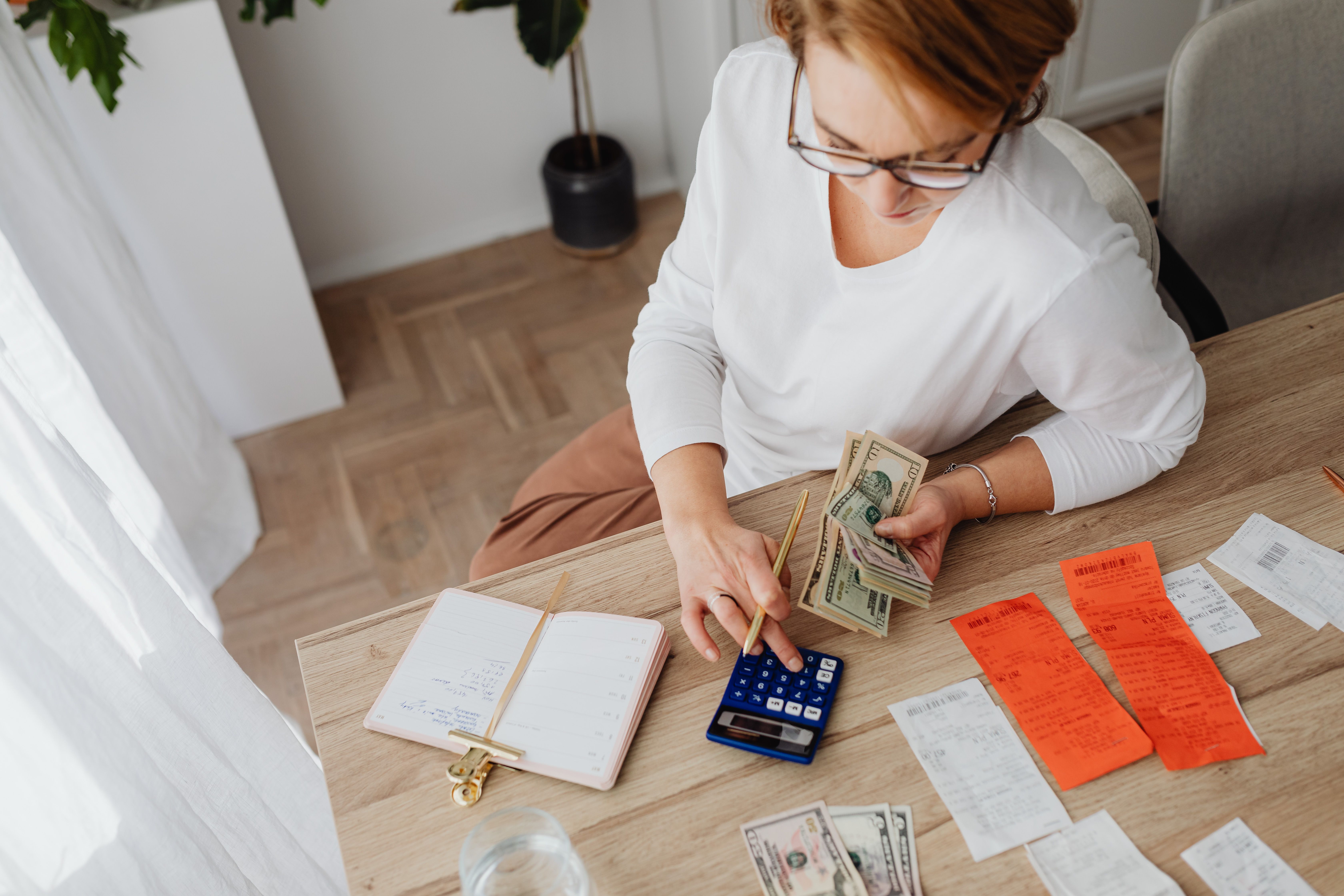 Top view of a woman managing household finances with a calculator, cash, and bills at home