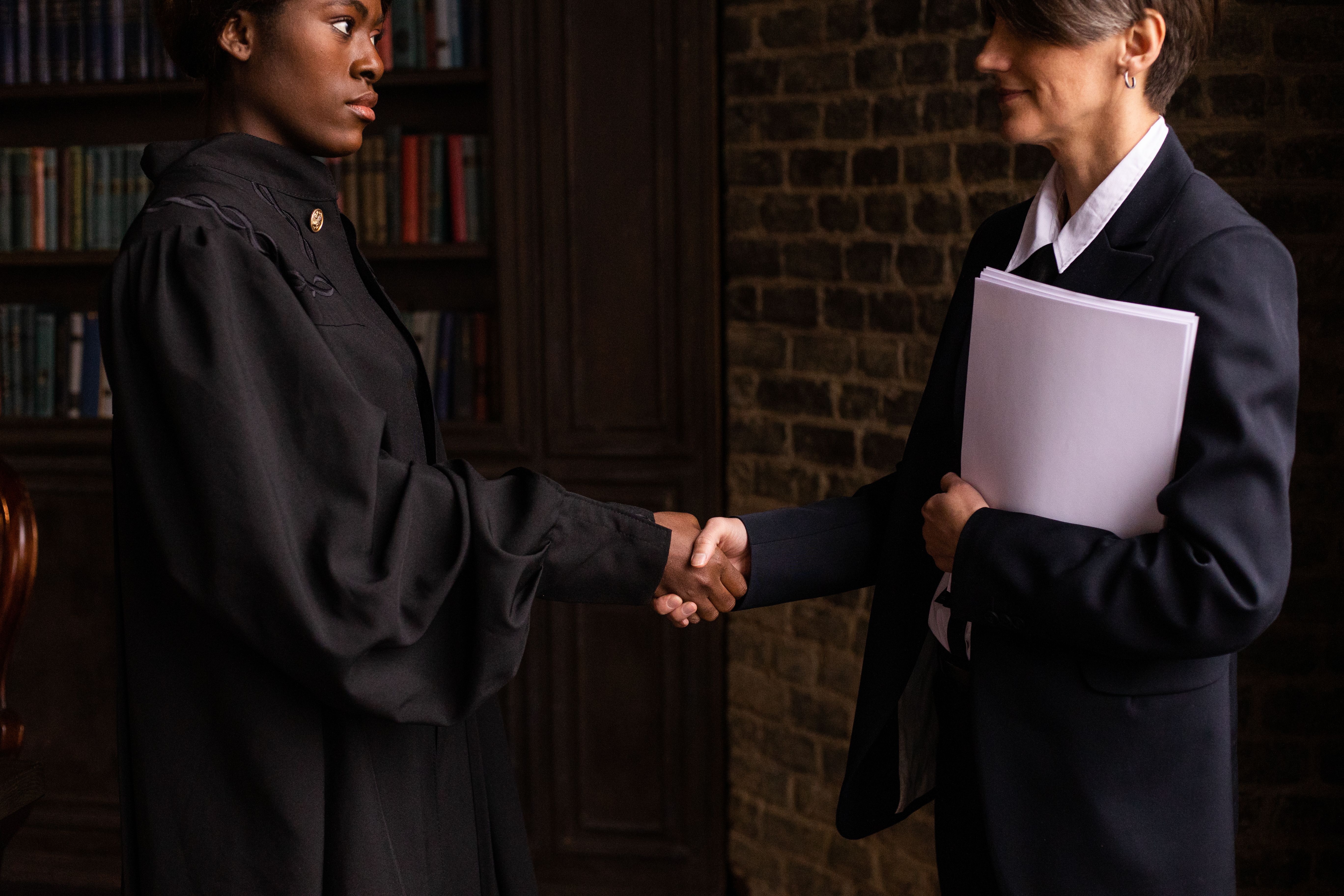 Lawyer in formal attire shaking hands with a client in a book-lined office to finalize a funding agreement