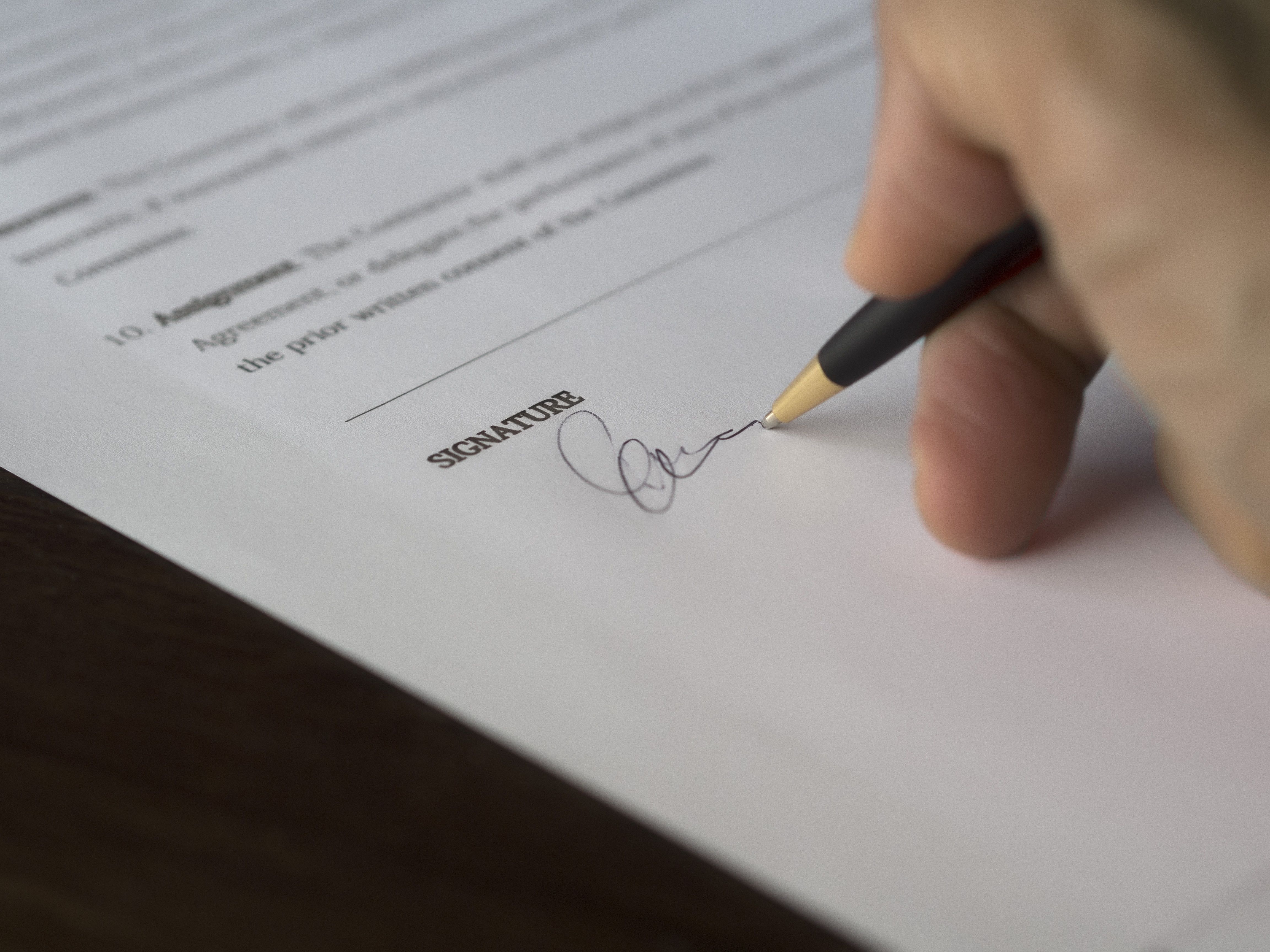 A hand signing a formal contract with a pen on a wooden desk
